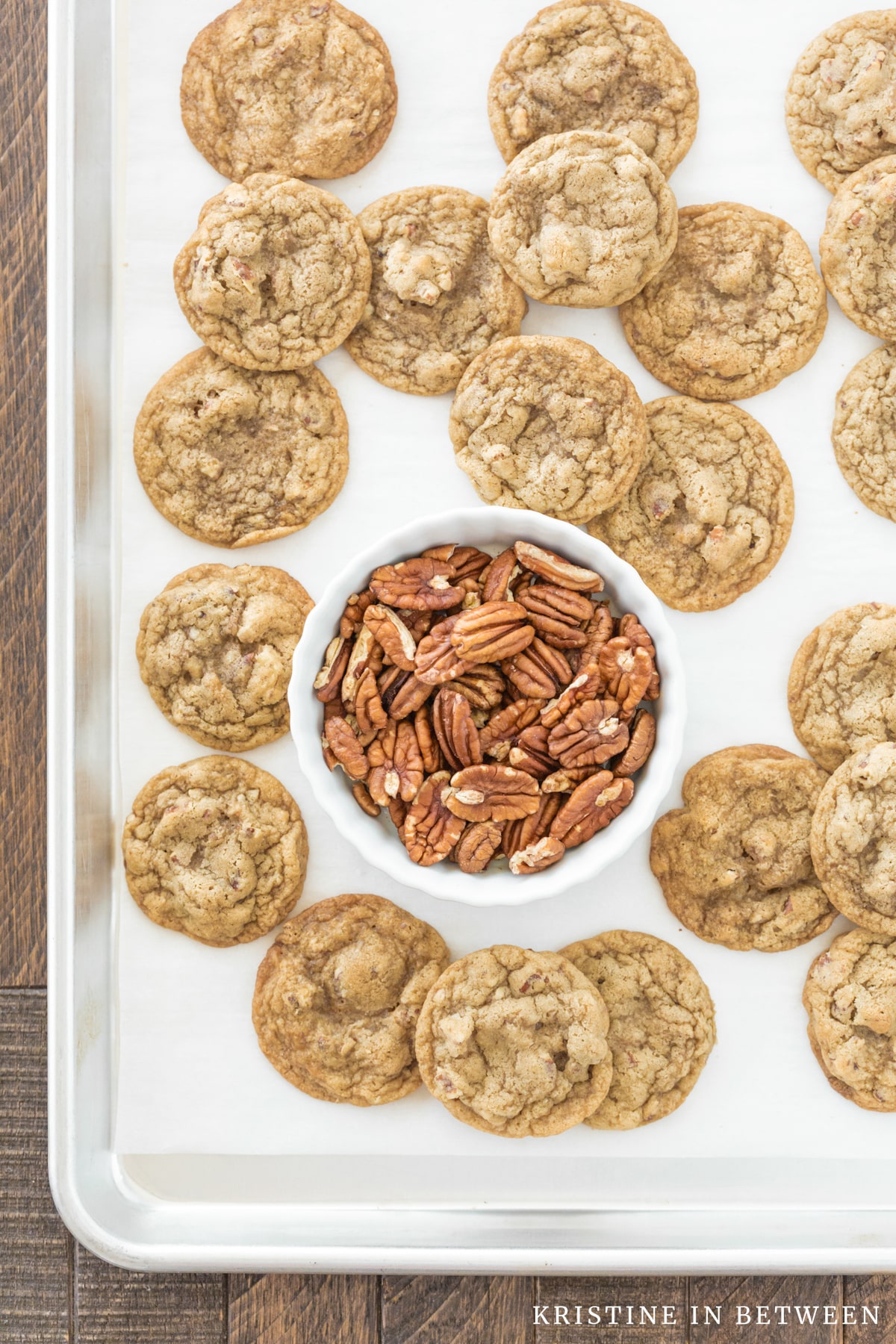 Pecan pie cookies laying on a cookie sheet with a small bowl of pecans.