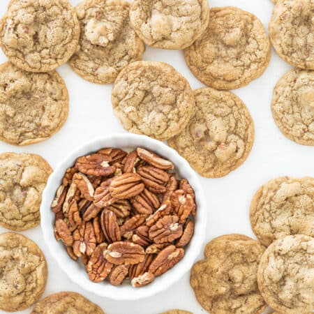 Cookies laying on a cookie sheet with a small bowl of pecans.
