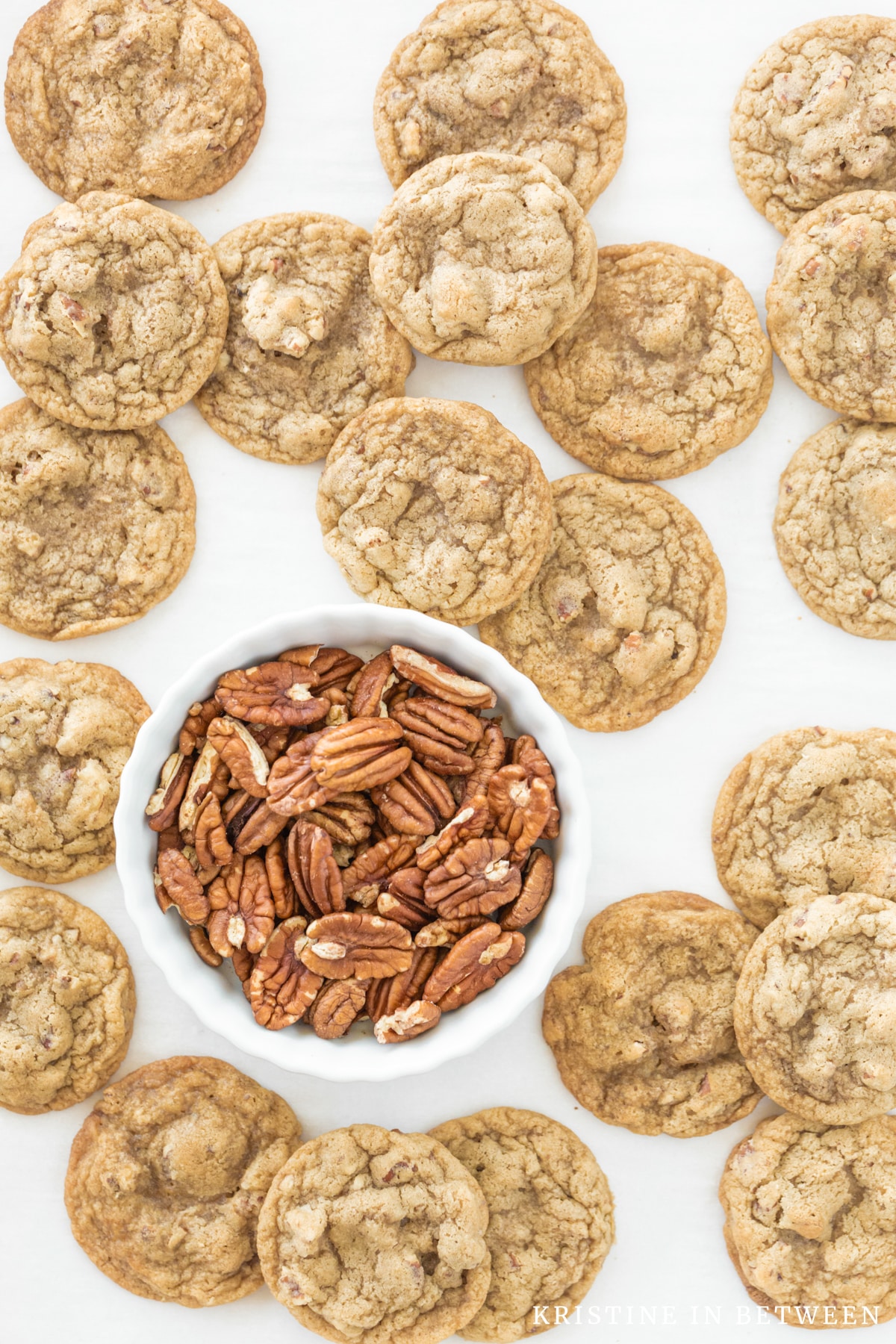 Cookies spread out on a baking sheet with a small bowl of pecans.