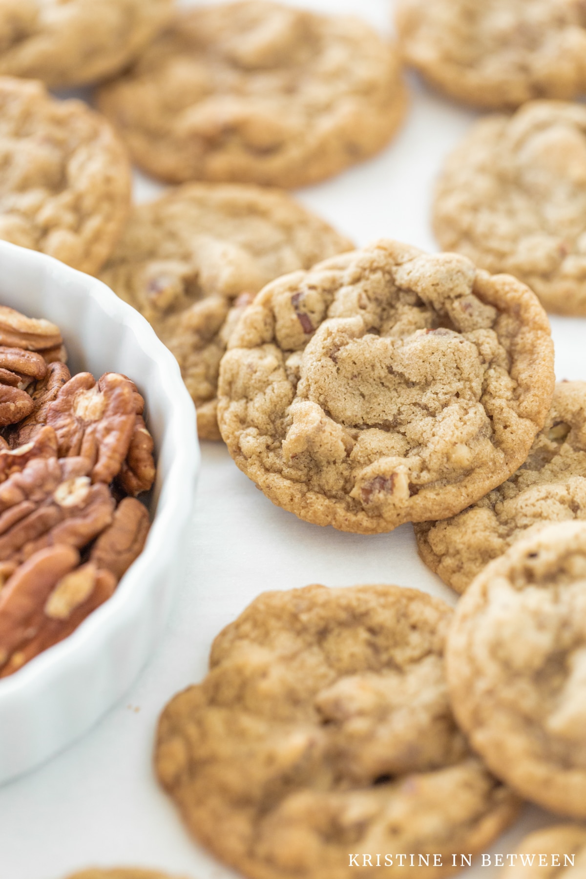 Cookies laying on a cookie sheet with a small bowl of pecans.