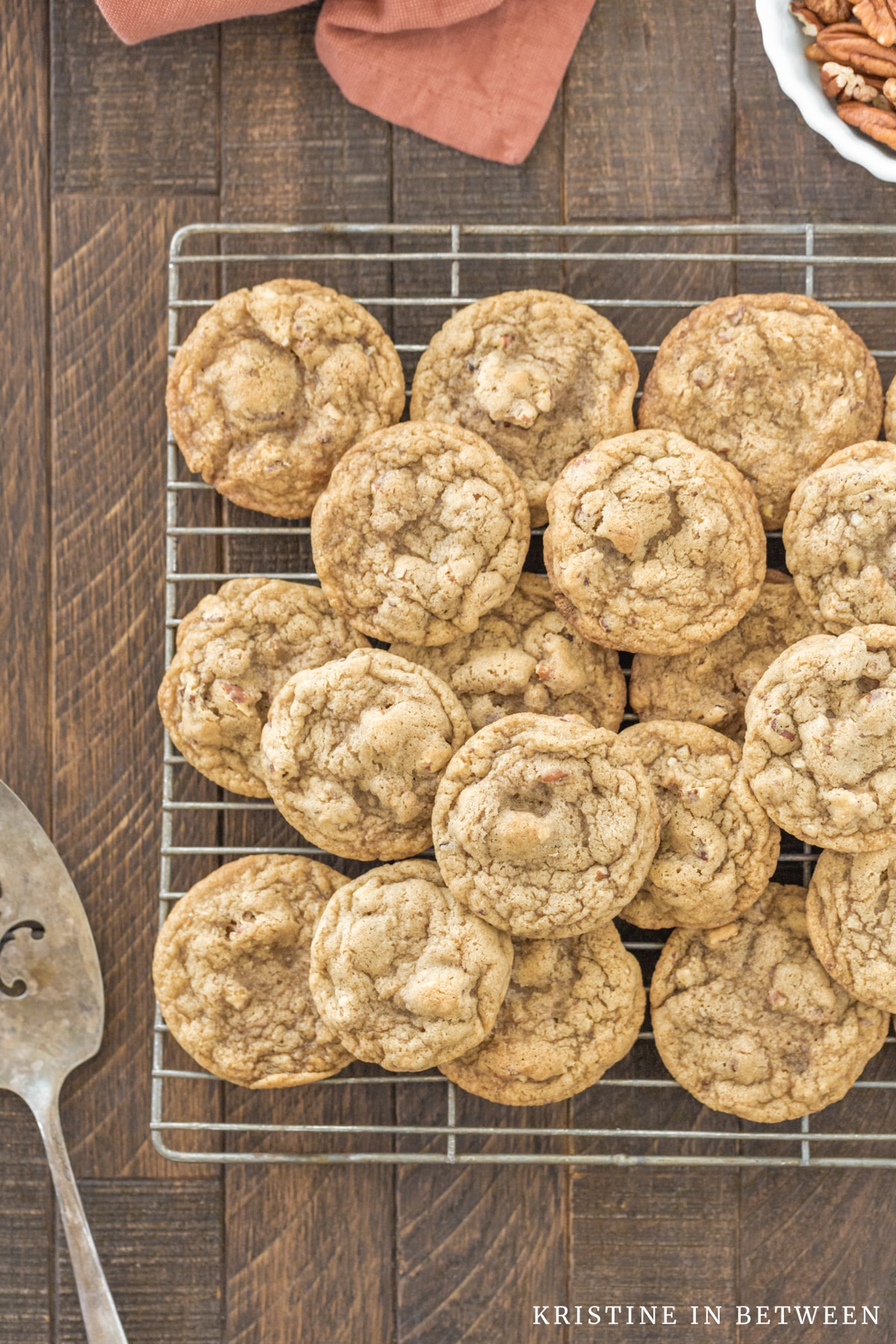 Cookies stacked up on a wire cooling rack with an old spatula laying next to them.