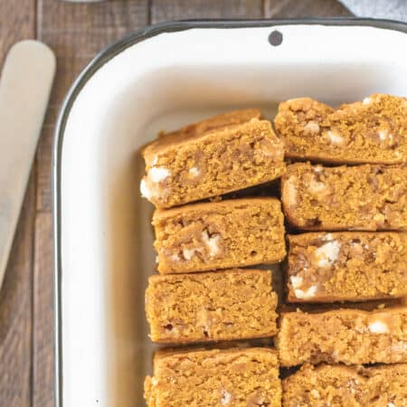 Blondies laying in a pan with a knife next to them and a cup of coffee in the background.