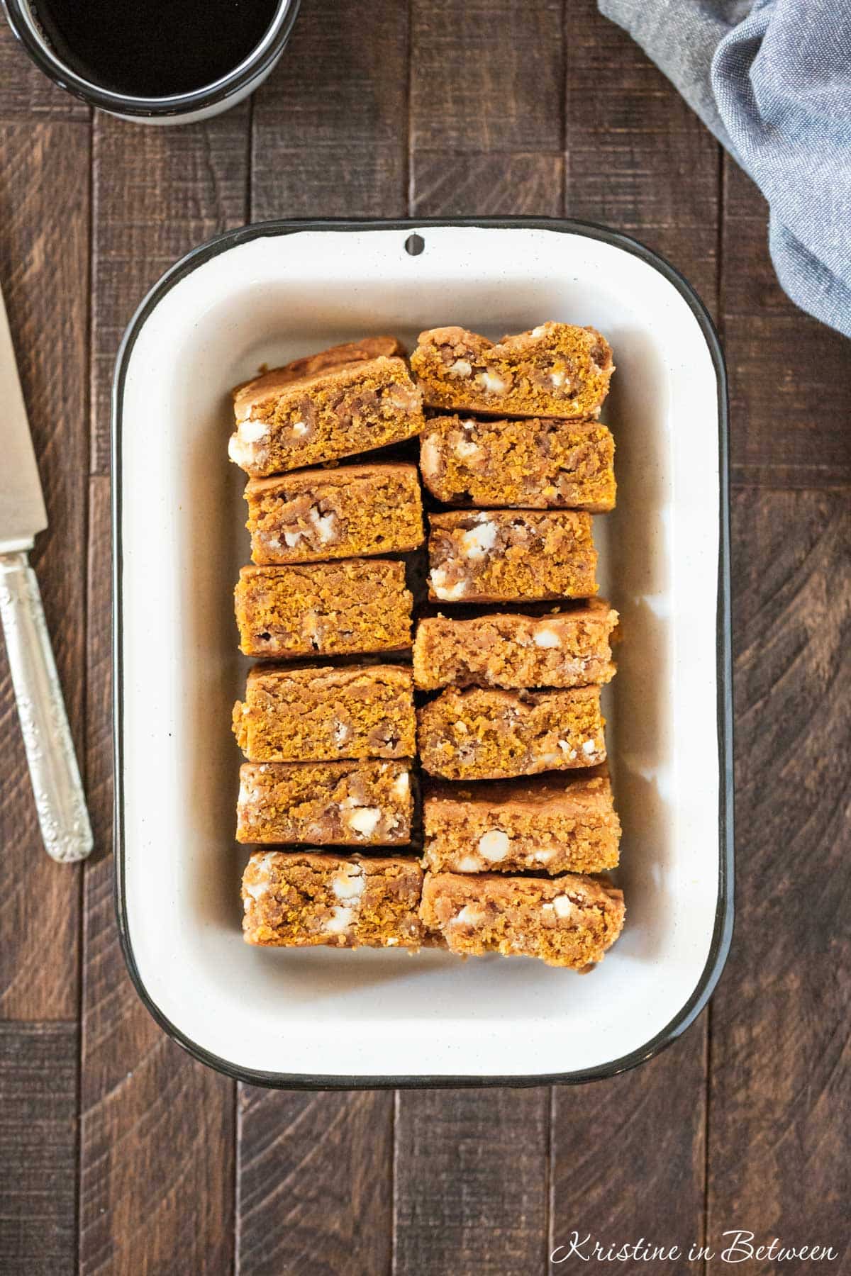 A pan of pumpkin blondies with white chocolate chips in them and a knife sitting next to them.