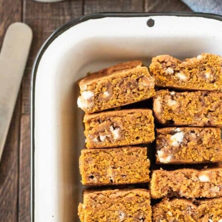 A pan of pumpkin blondies with white chocolate chips in them and a knife sitting next to them.