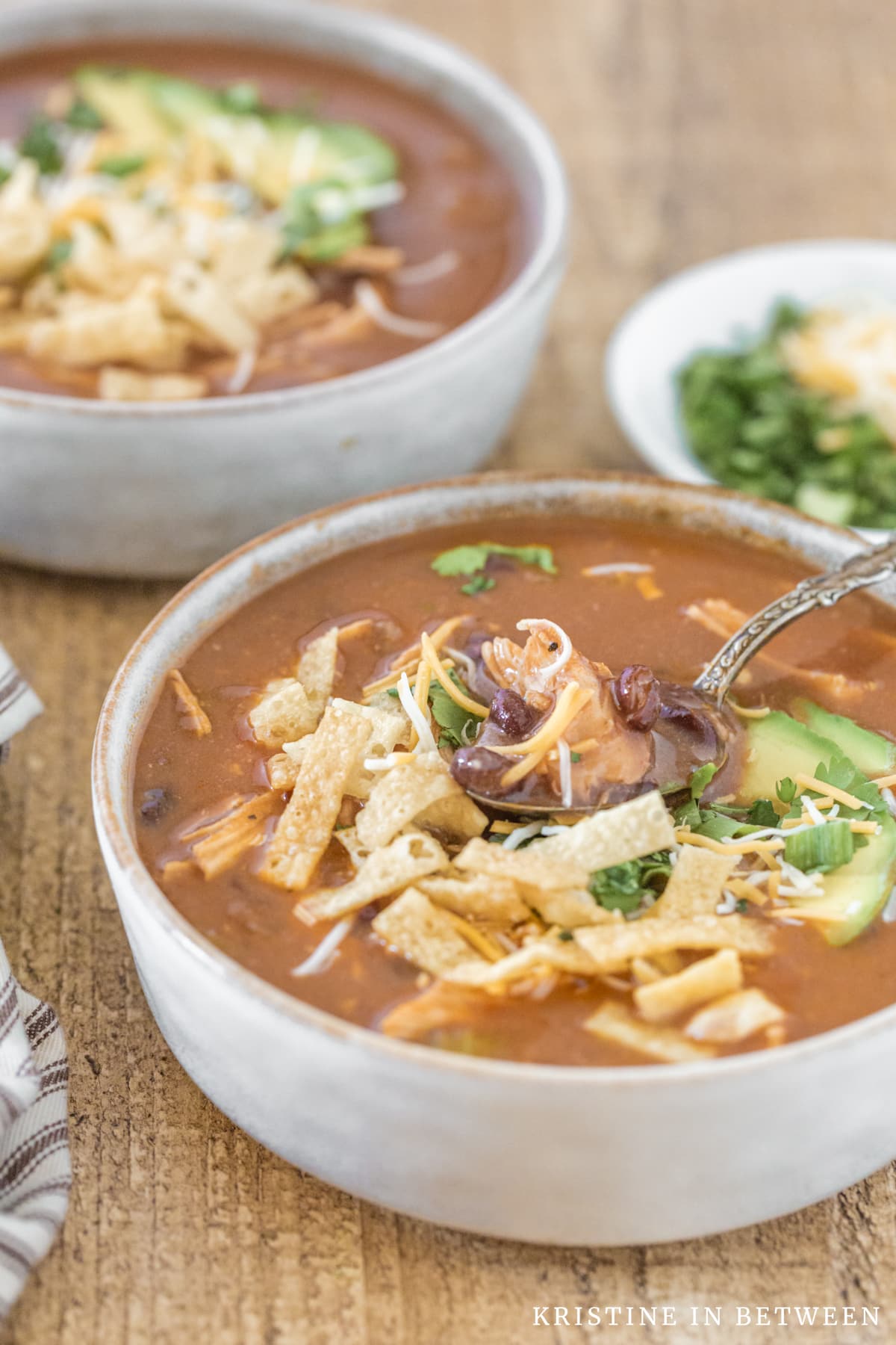 A bowl of enchilada soup with a bite on the spoon and another bowl in the background.