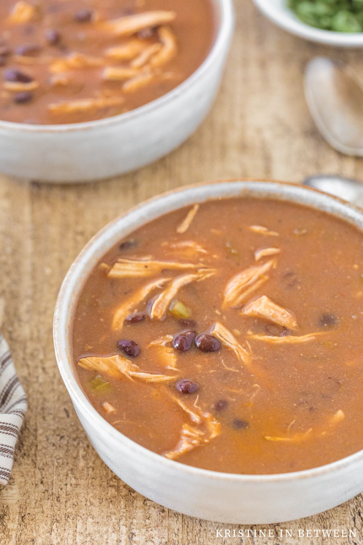 A bowl of enchilada soup with spoons in the background.