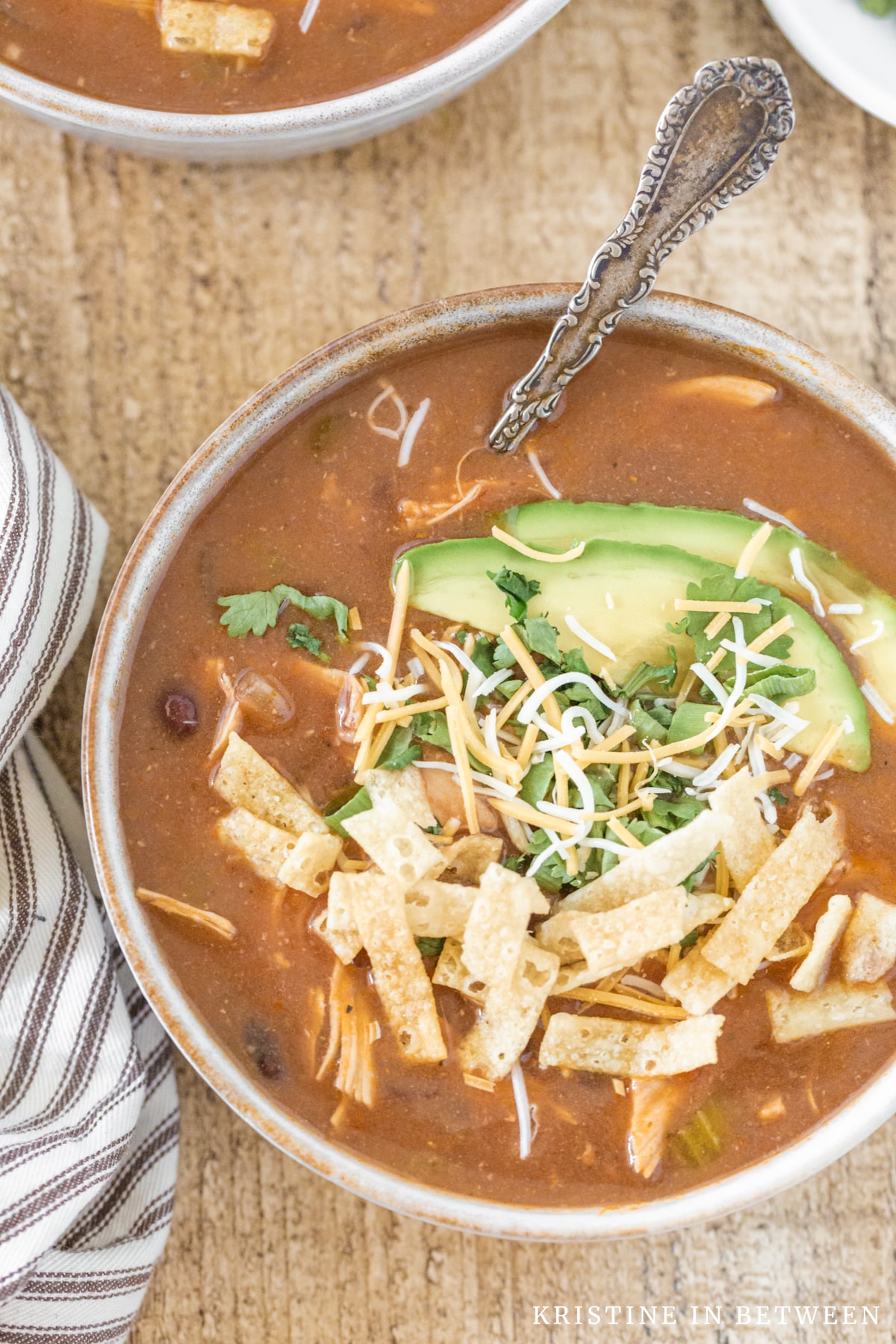 A bowl of chicken enchilada soup topped with cheese, tortilla strips, and avocado.
