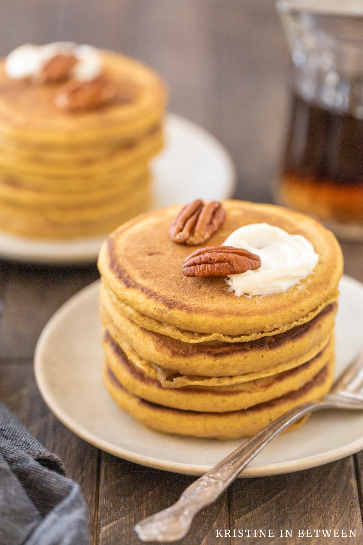 Four pancakes stacked up on a white plate with pecans and butter on top.