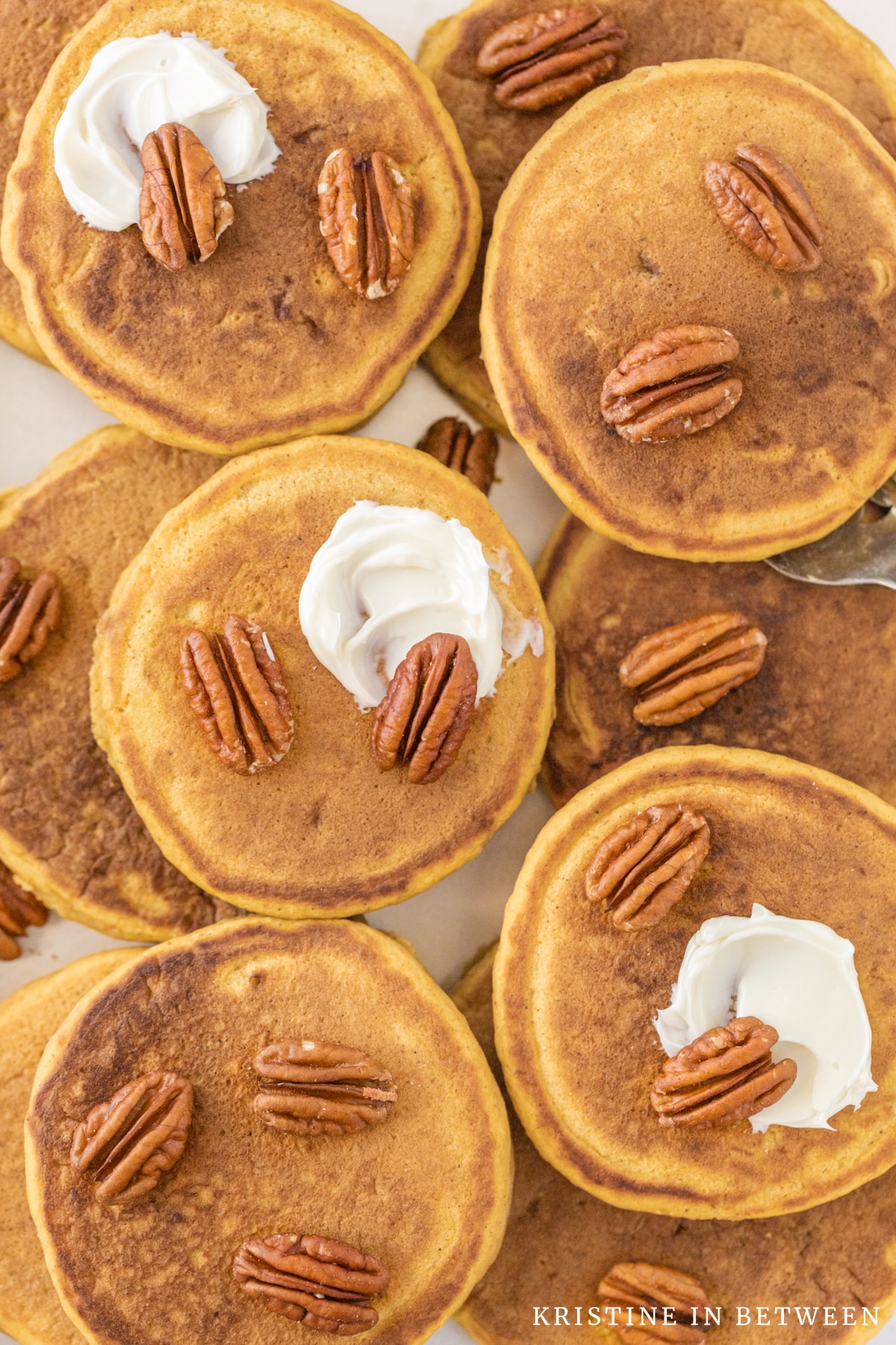 Pancakes piled up on top of each other with pecans and butter on top.