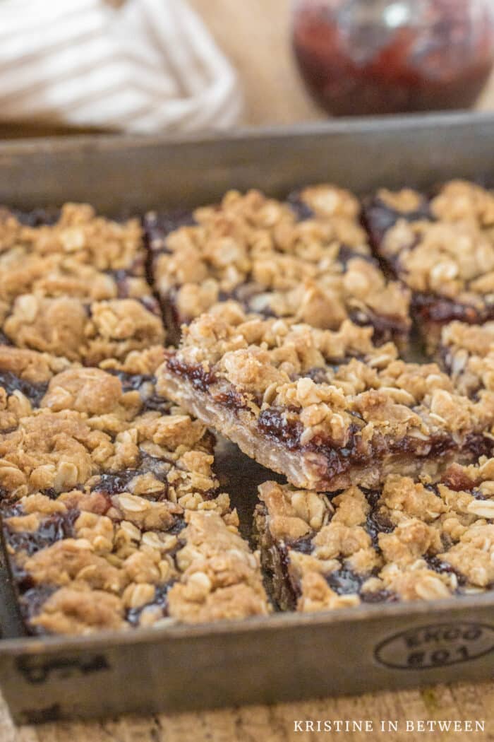 Raspberry jam crumble bars sitting in an antique baking pan with an old spatula.