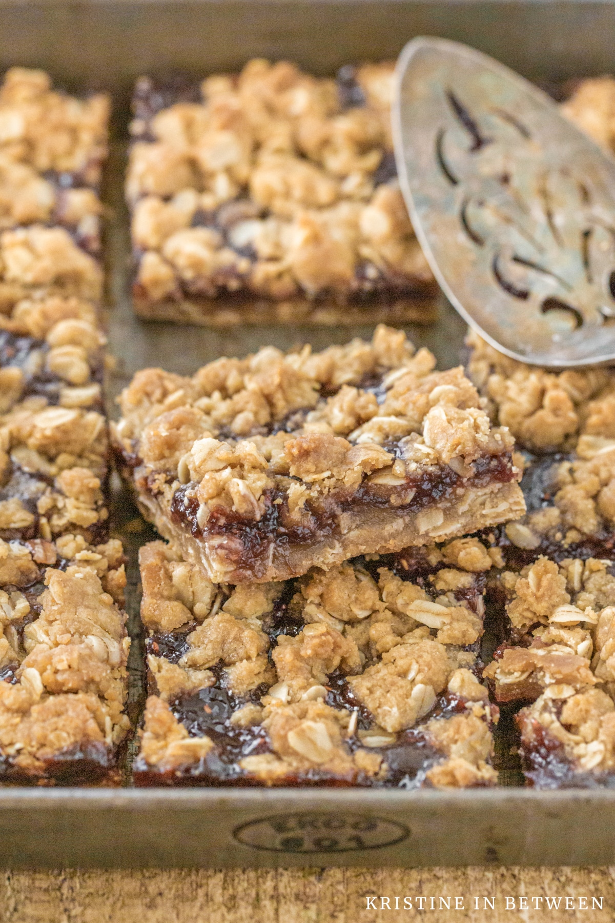 Raspberry jam crumble bars sitting in an antique baking pan with an old spatula.