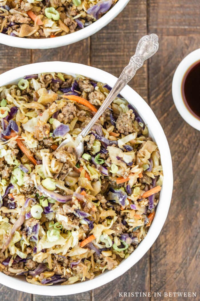 Sausage and cabbage in a white bowl with a fork in it and a small dish of soy sauce in the background.