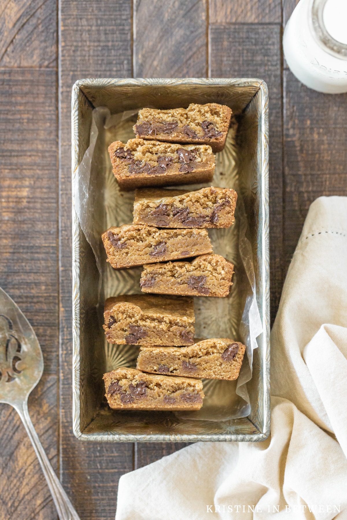 Chocolate chip cookie bars stacked up in an antique tin with a napkin next to them.