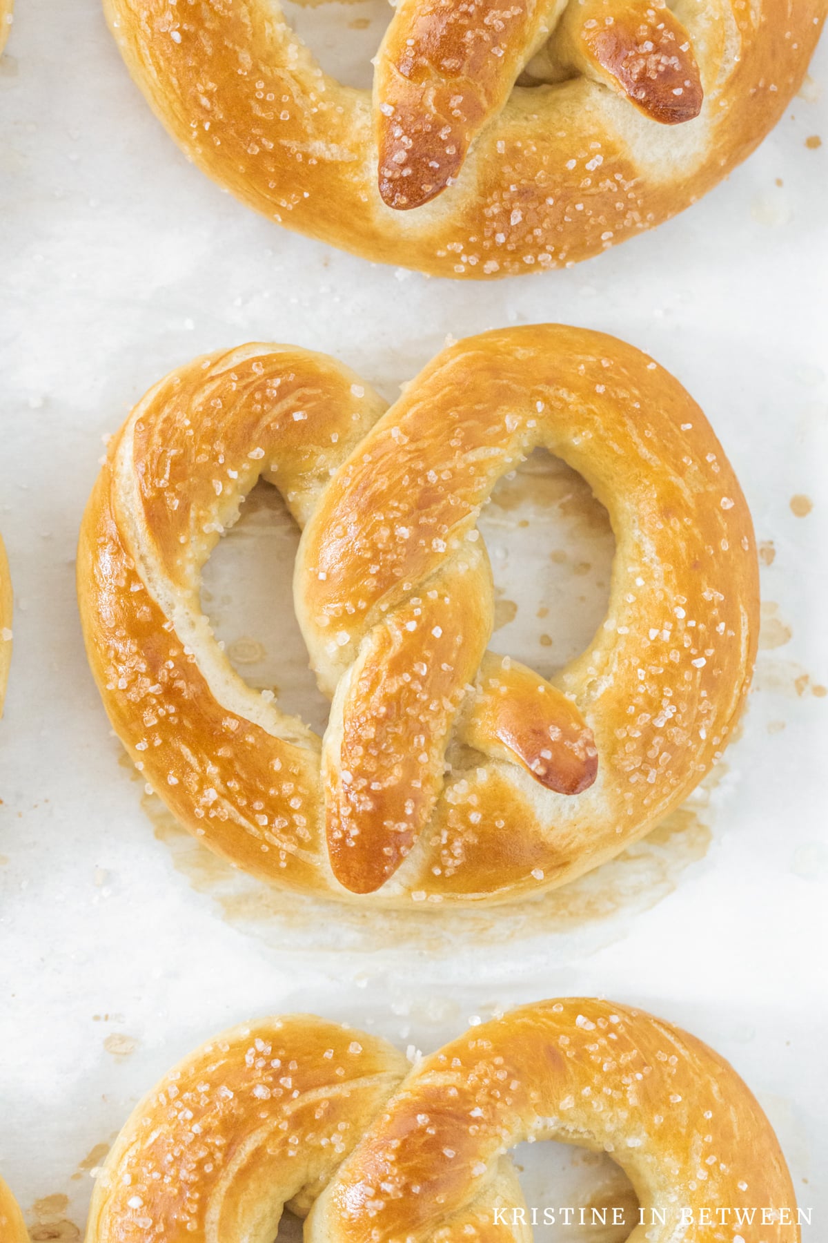 A salted pretzel sitting on  the baking pan with two other pretzels.