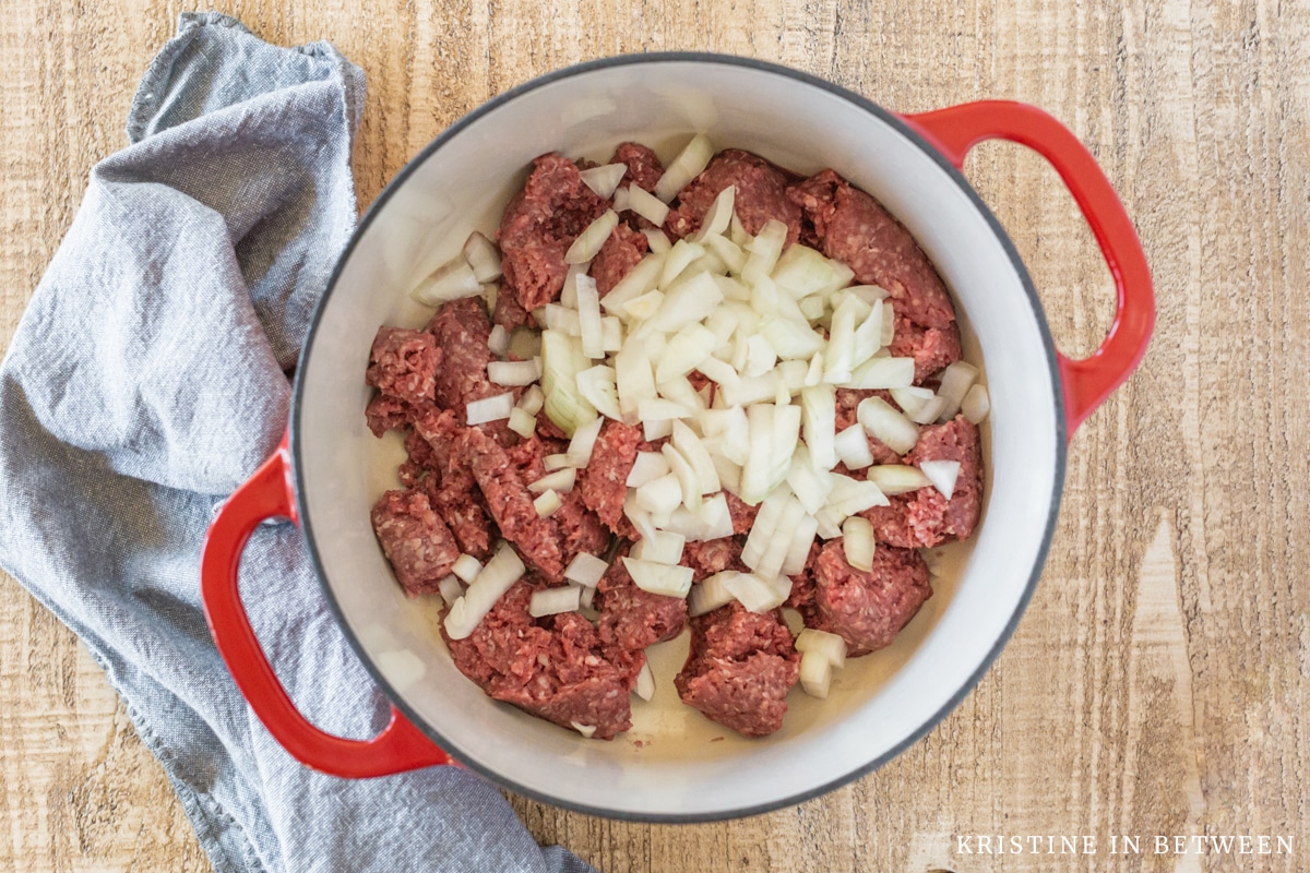 Hamburger and onions in a red Dutch oven.