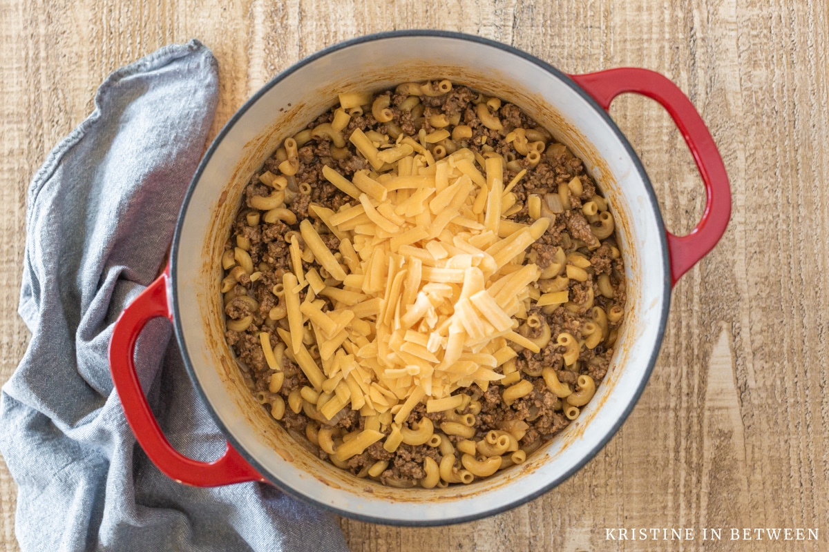 Cheese added to the top of cooked beef and onions in a red Dutch oven.