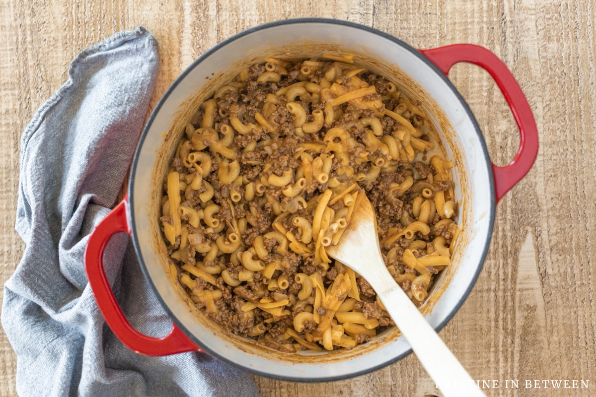 A wooden spoon in a red Dutch oven with cooked chili mac.