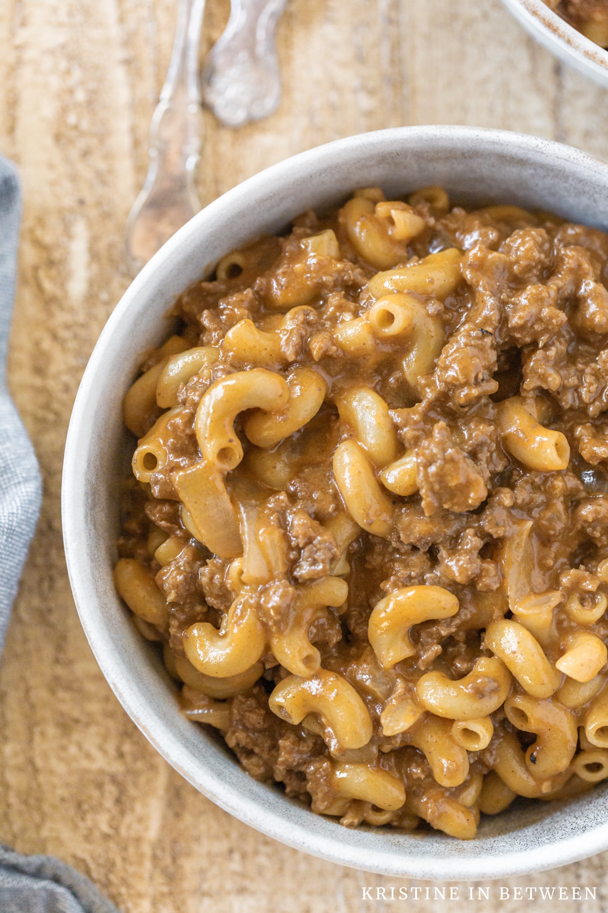 A bowl of chili mac sitting on a wooden table with a blue napkin.