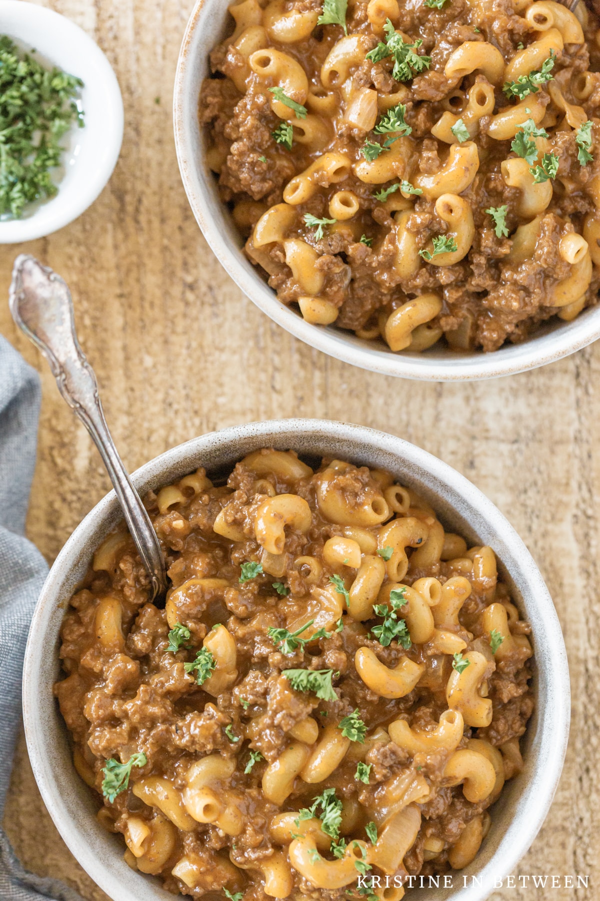 Two bowls of chili mac topped with fresh parsley sitting with a blue napkin.