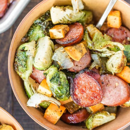 A bowl of Kielbasa sausage and Brussel sprouts with a fork in it.