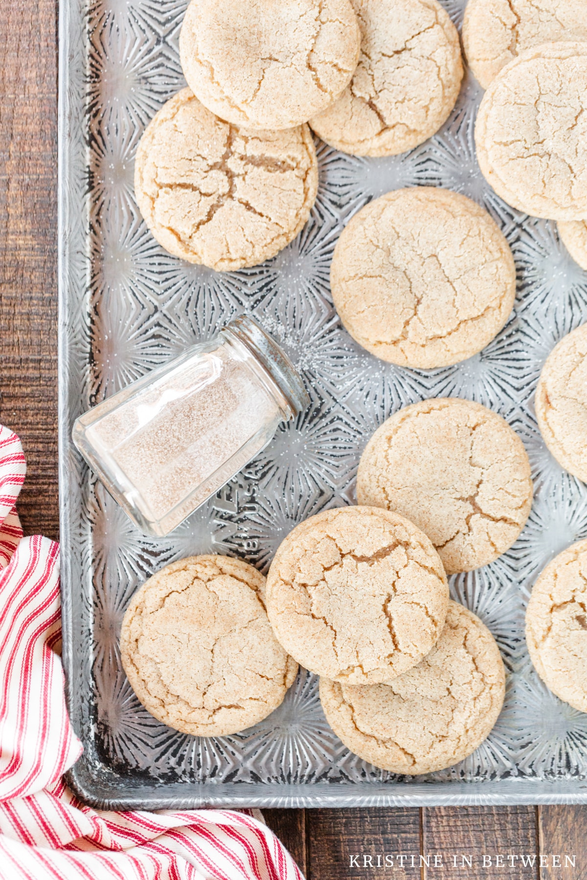 Snickerdoodle cookies laying on an old cookie sheet with a shaker full of sugar and a red striped napkin.