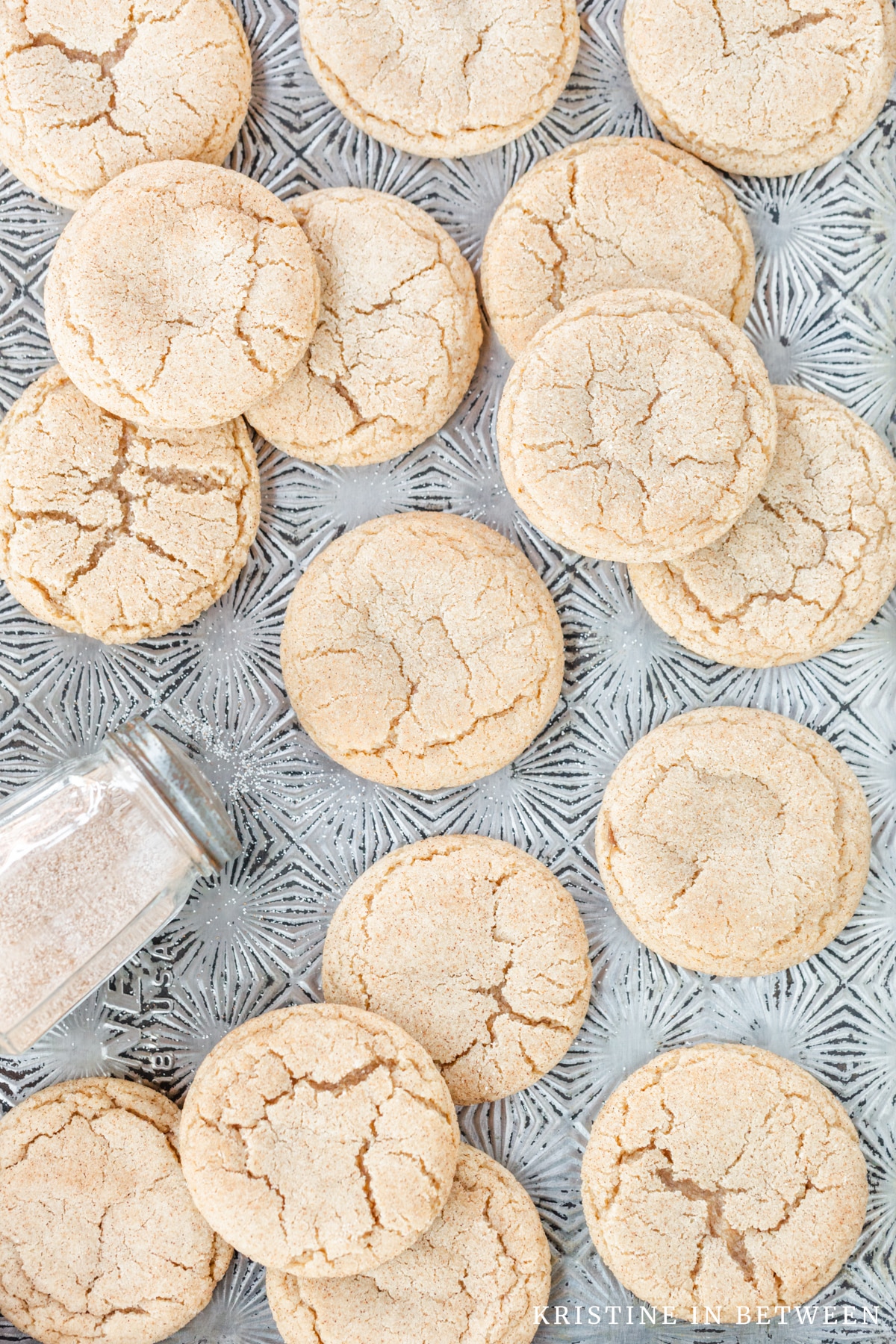 Cookies laying on an antique cookie sheet with a shaker full of sugar.