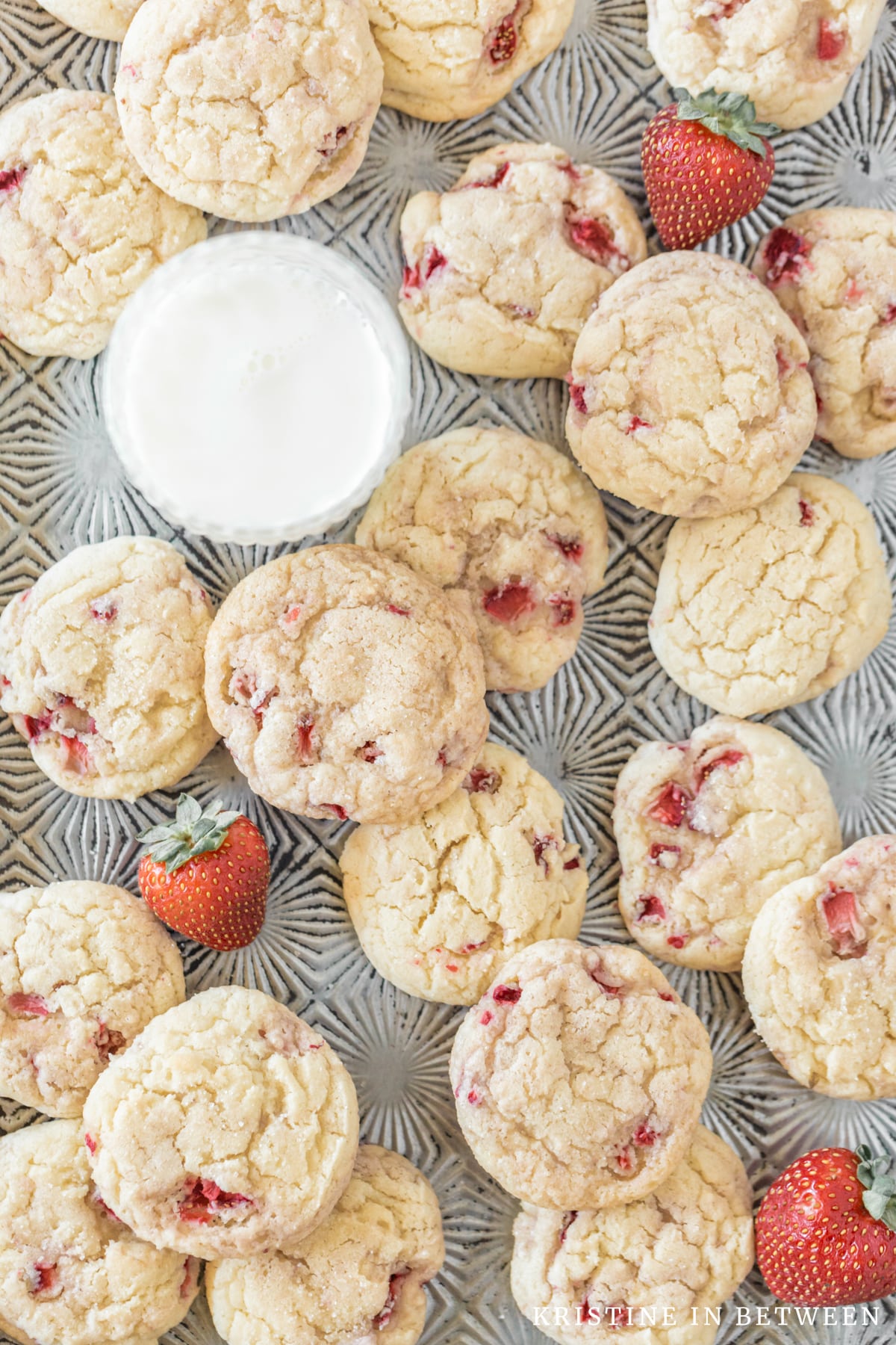 Strawberry sugar cookies laying on an antique cookie sheet with a glass of milk.