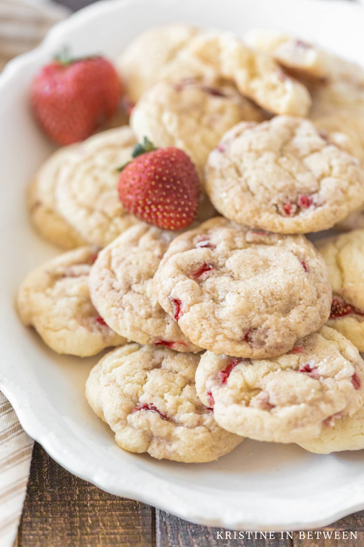 Strawberry cookies piled up on a white platter with two strawberries.