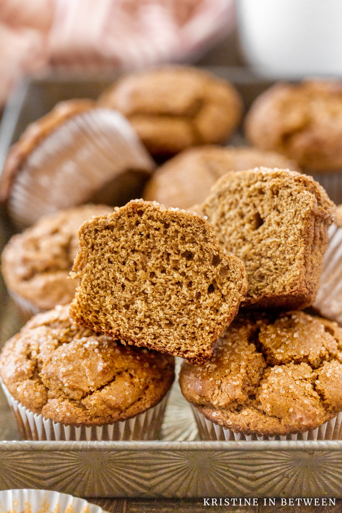 A muffin pan full of gingerbread muffins with one cut in half.