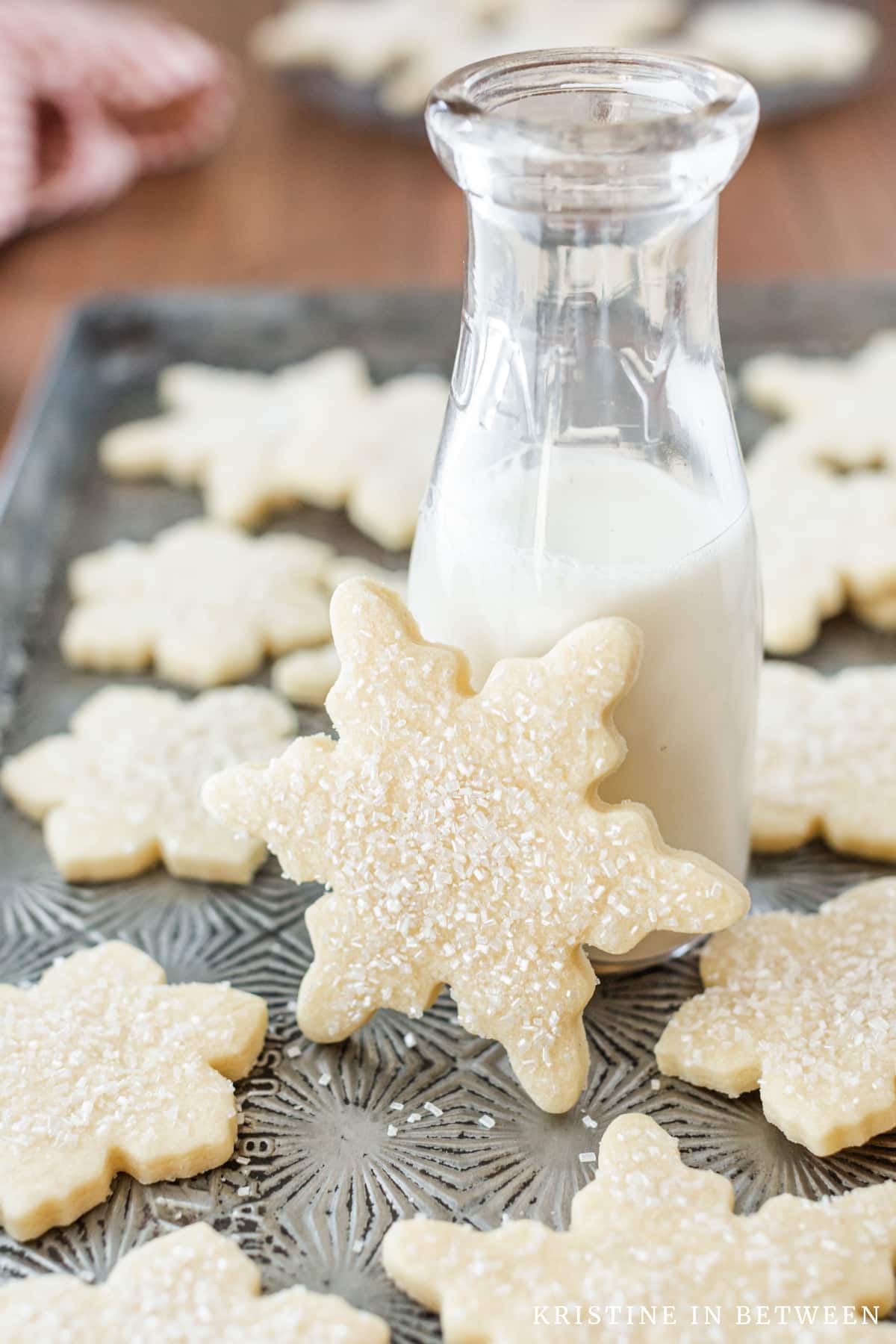 Cut out sugar cookies laying on an old cookie sheet with one leaning up on a jar of milk.