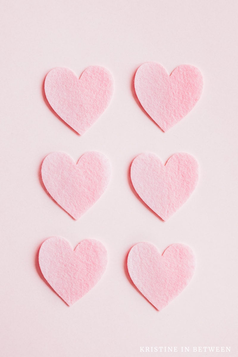 Pink felt hearts laying on a pink background.
