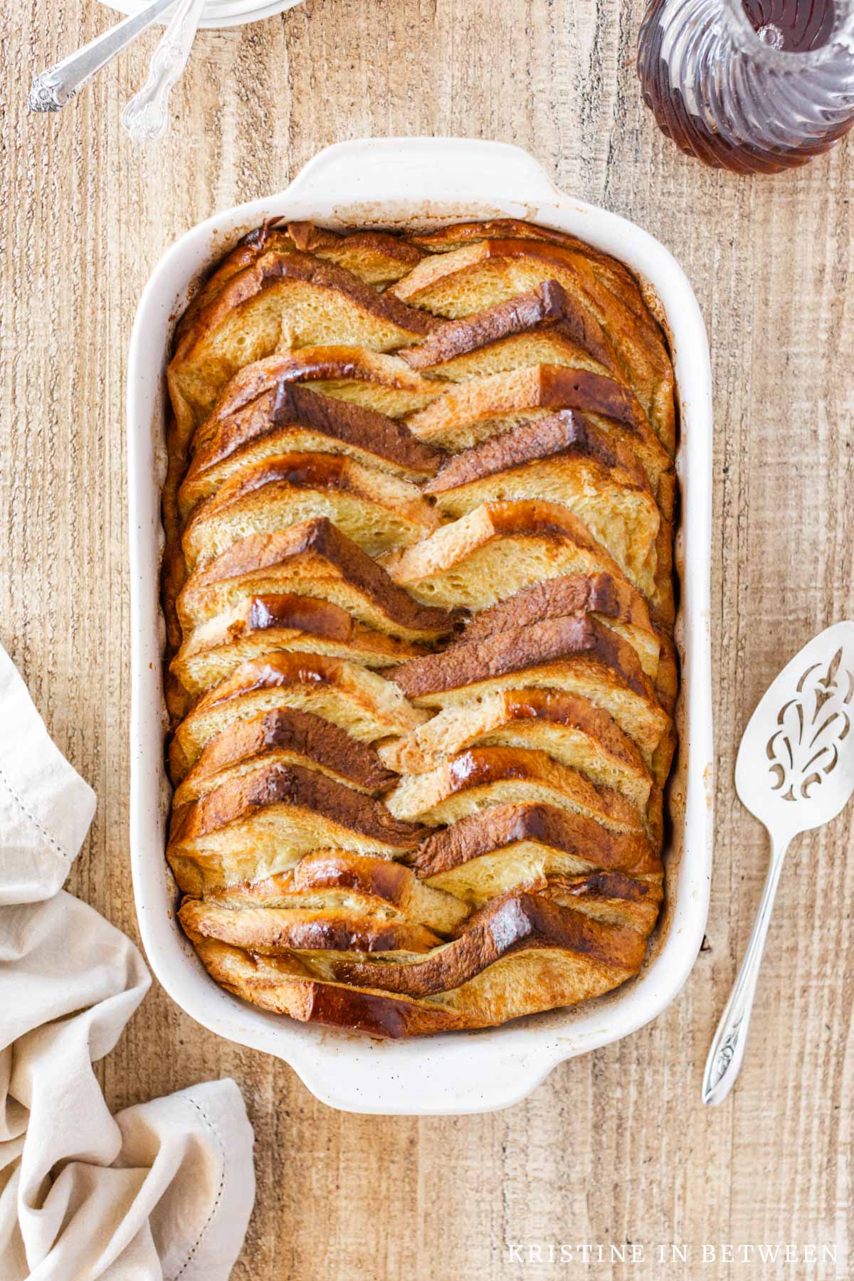 Baked French toast in a casserole dish with syrup and a spatula in the background.