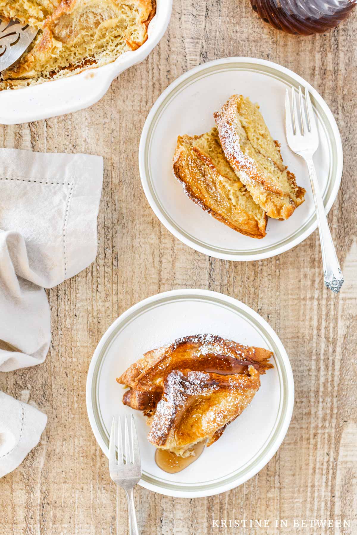 Two plates of baked French toast with forks and a beige napkin sitting next to them.