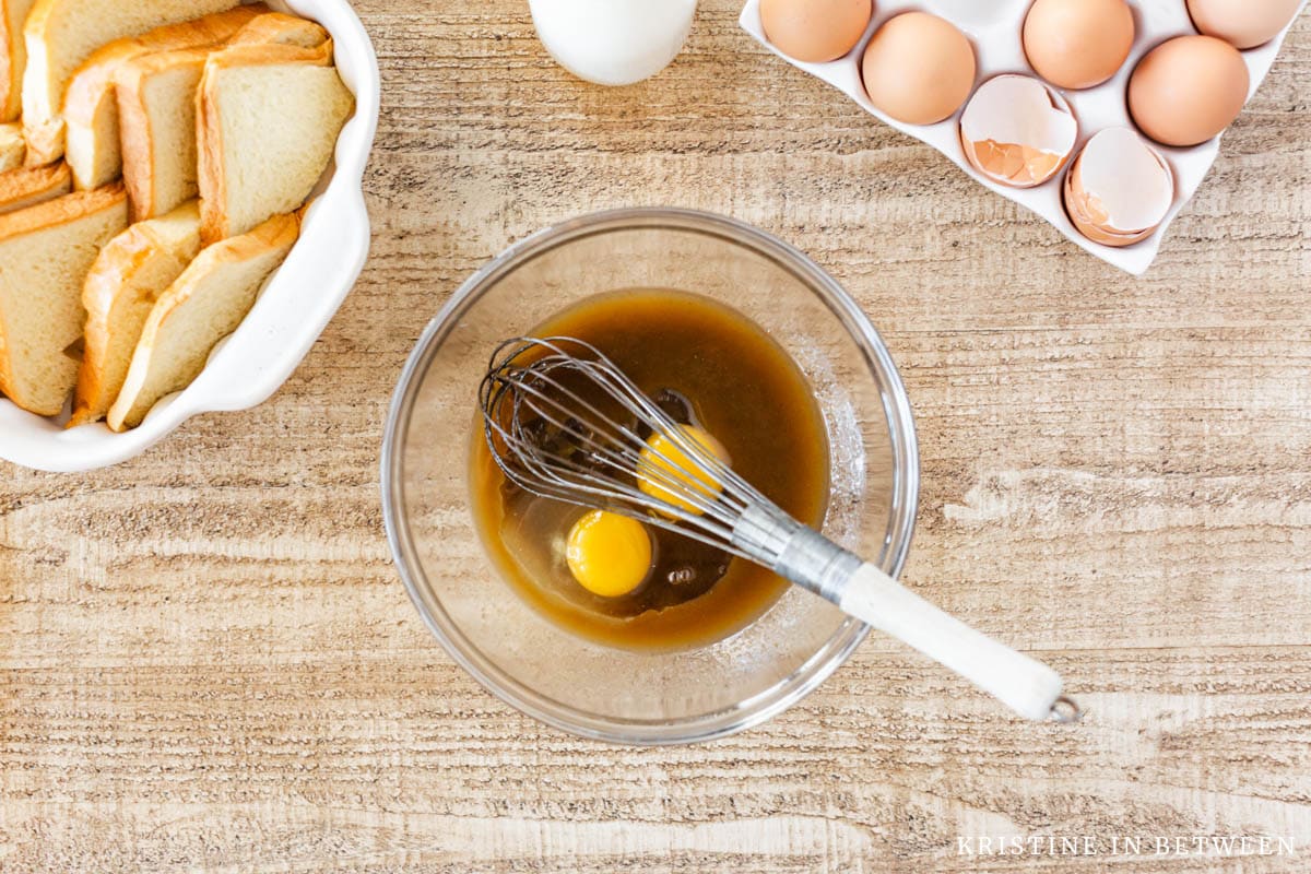 A bowl of melted butter with two eggs cracked in it and a whisk.
