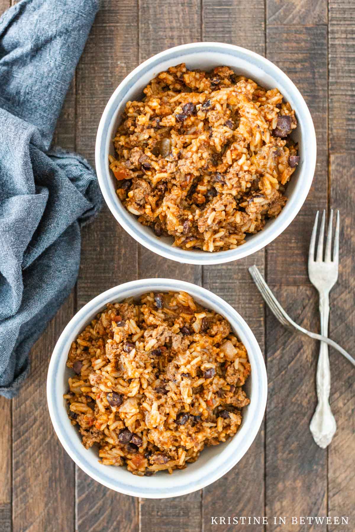 Two bowls of casserole with no toppings in white bowls with two forks sitting next to them.