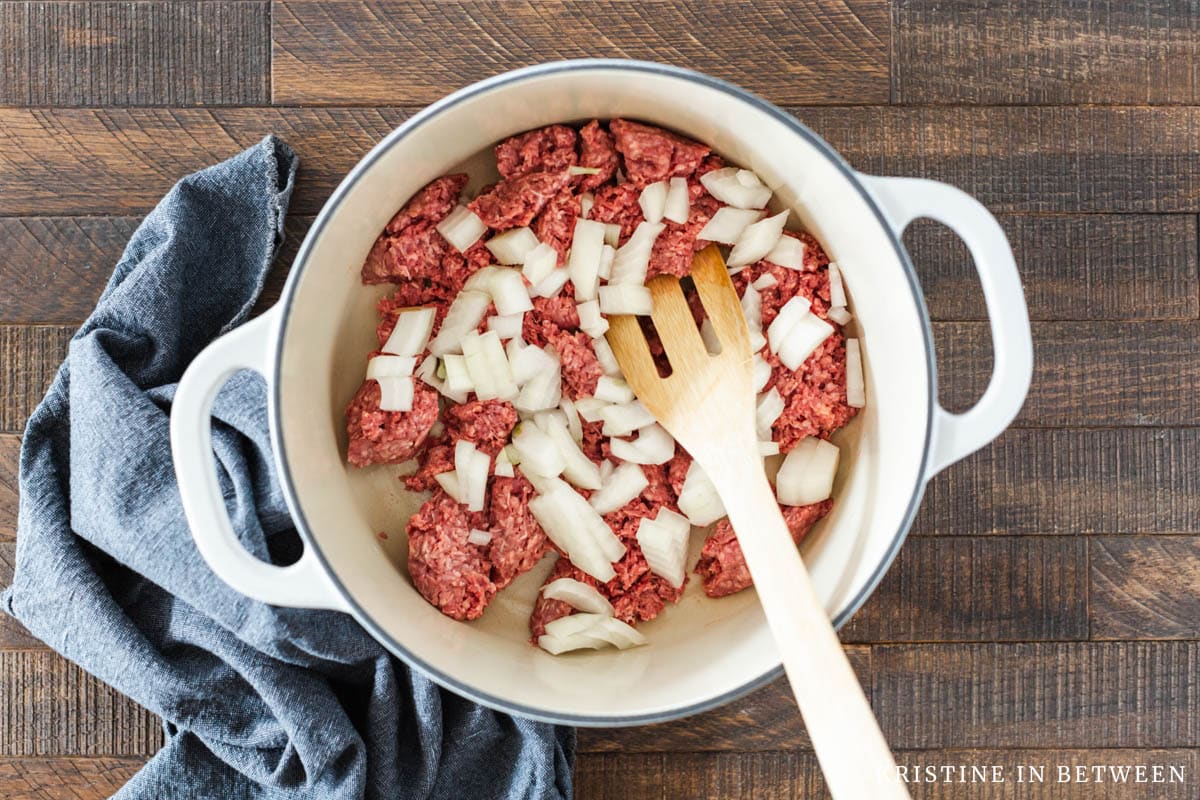 Raw hamburger meat and a chopped up onion in a Dutch oven ready for cooking.