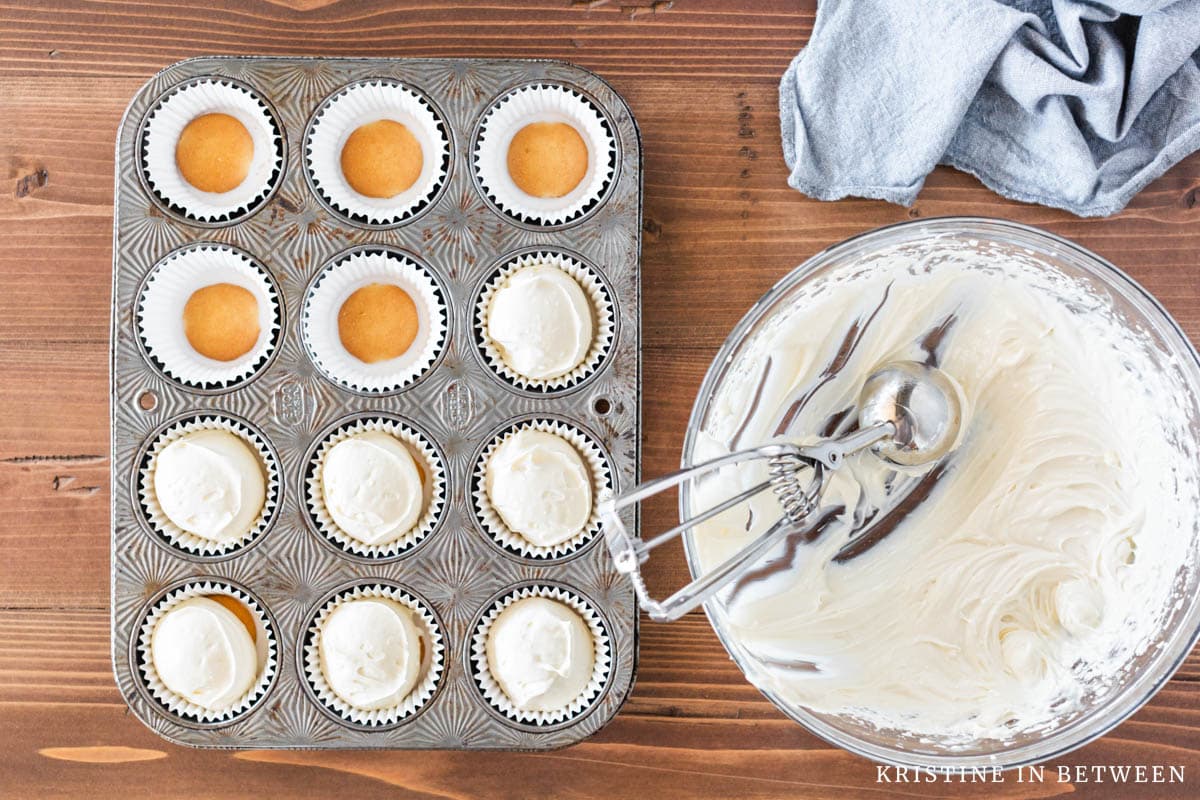 A muffin tin partway full of cream cheese tarts with a bowl and a scoop laying next to it.