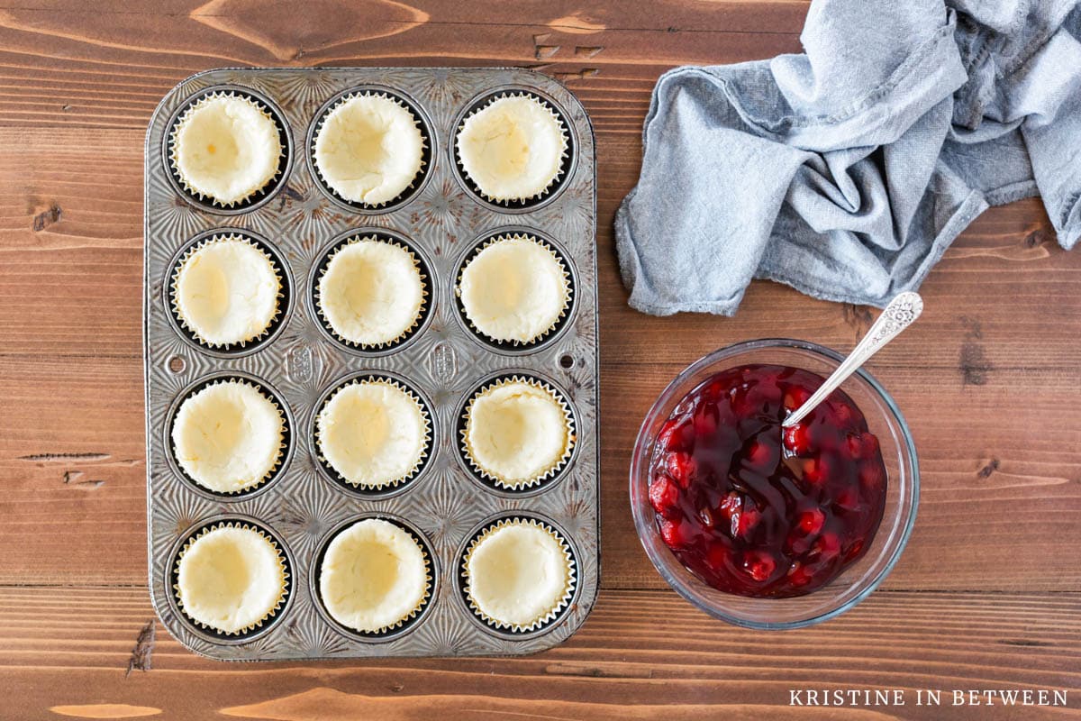 Cream cheese tarts after they've been baked sitting with a bowl of cherry pie filling.