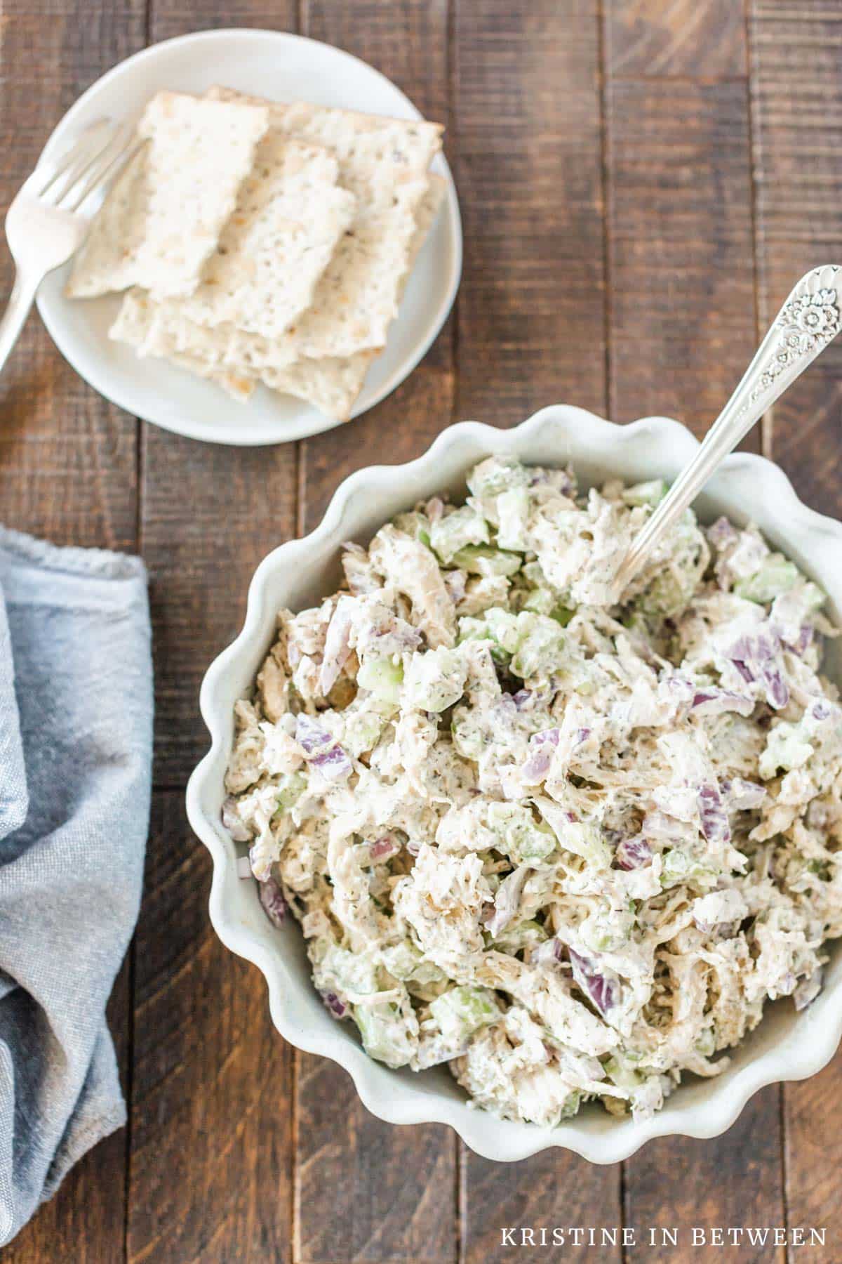 Chicken salad in a bowl with some crackers in the background.