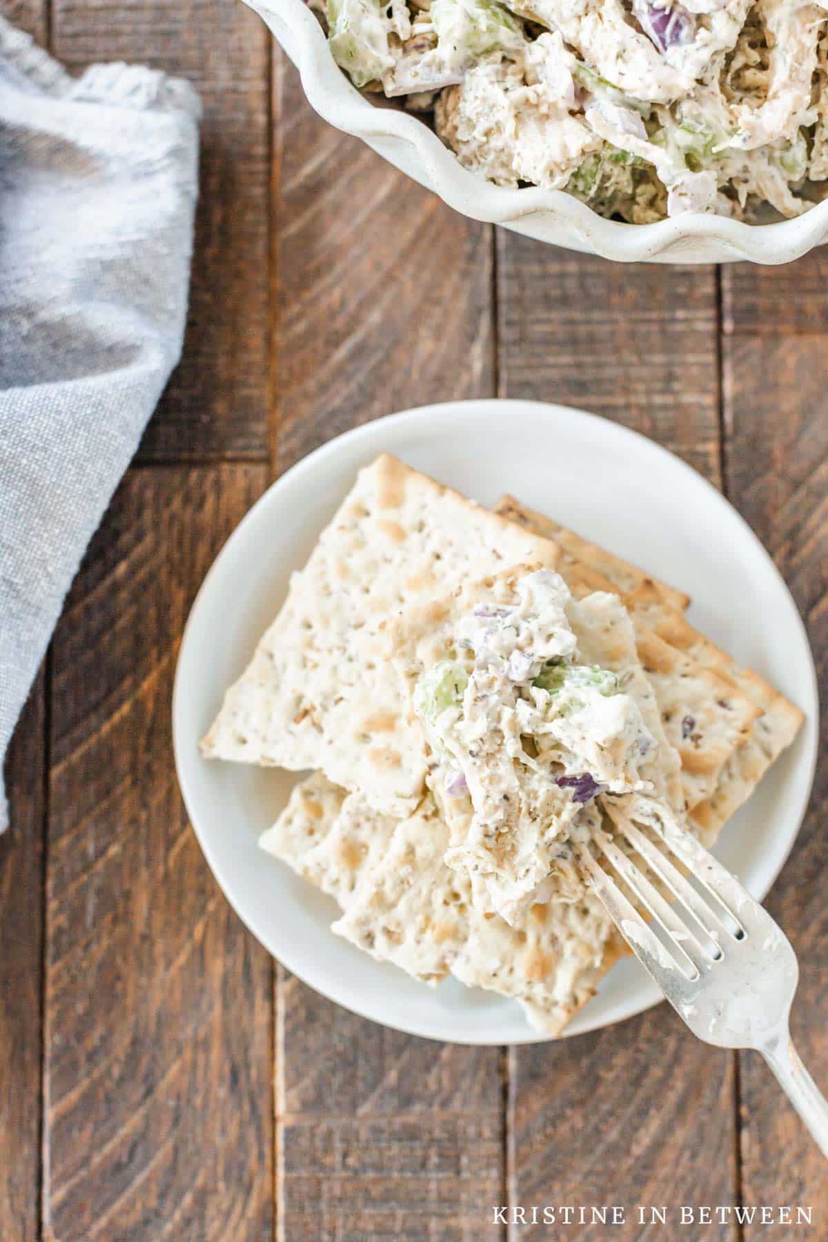 A bite of chicken salad sitting on top of crackers with a fork sitting next to it.