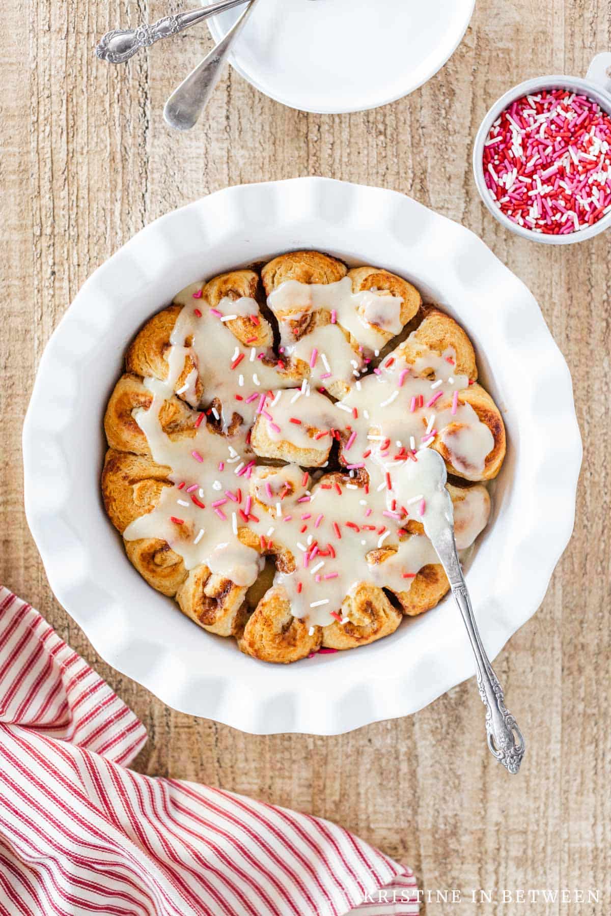 Cinnamon rolls in a round dish with frosting and sprinkles.