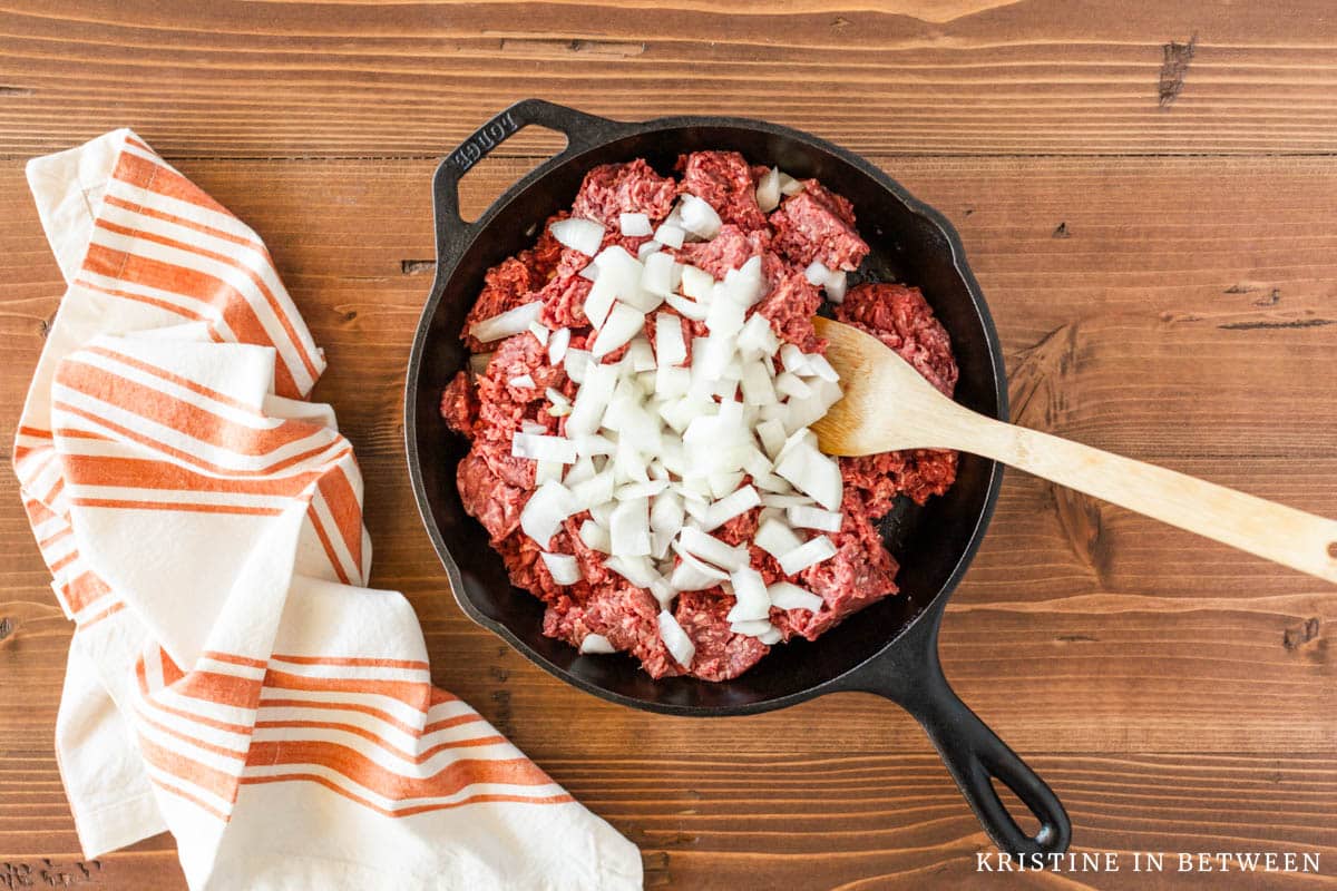 Ground beef and chopped onion in a cast iron pan ready to be cooked.