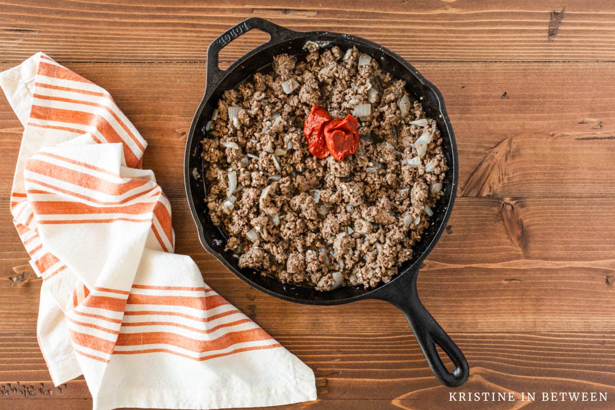 Cooked beef and onion in a cast iron skillet with tomato sauce and beef broth. 