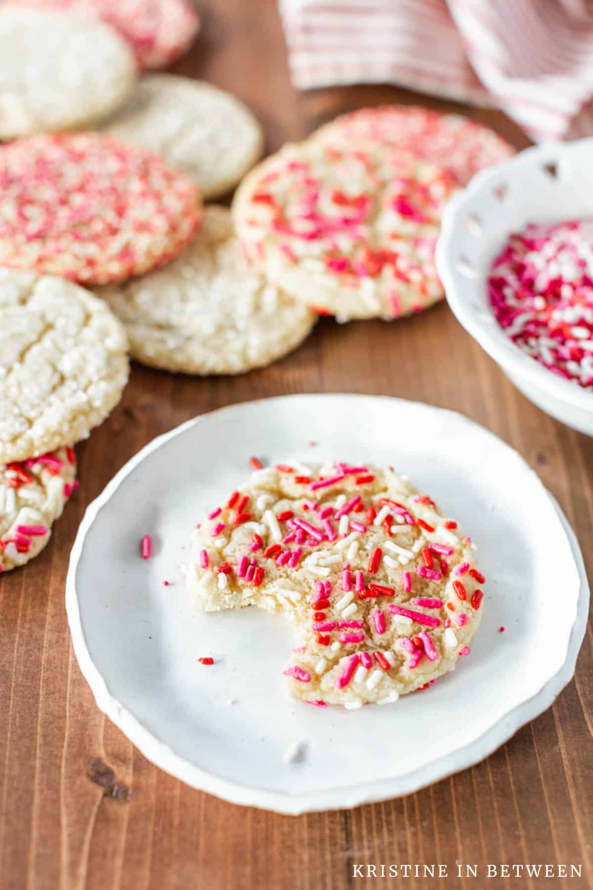 A sprinkle sugar cookie laying on a small white plate with a bite out of it.