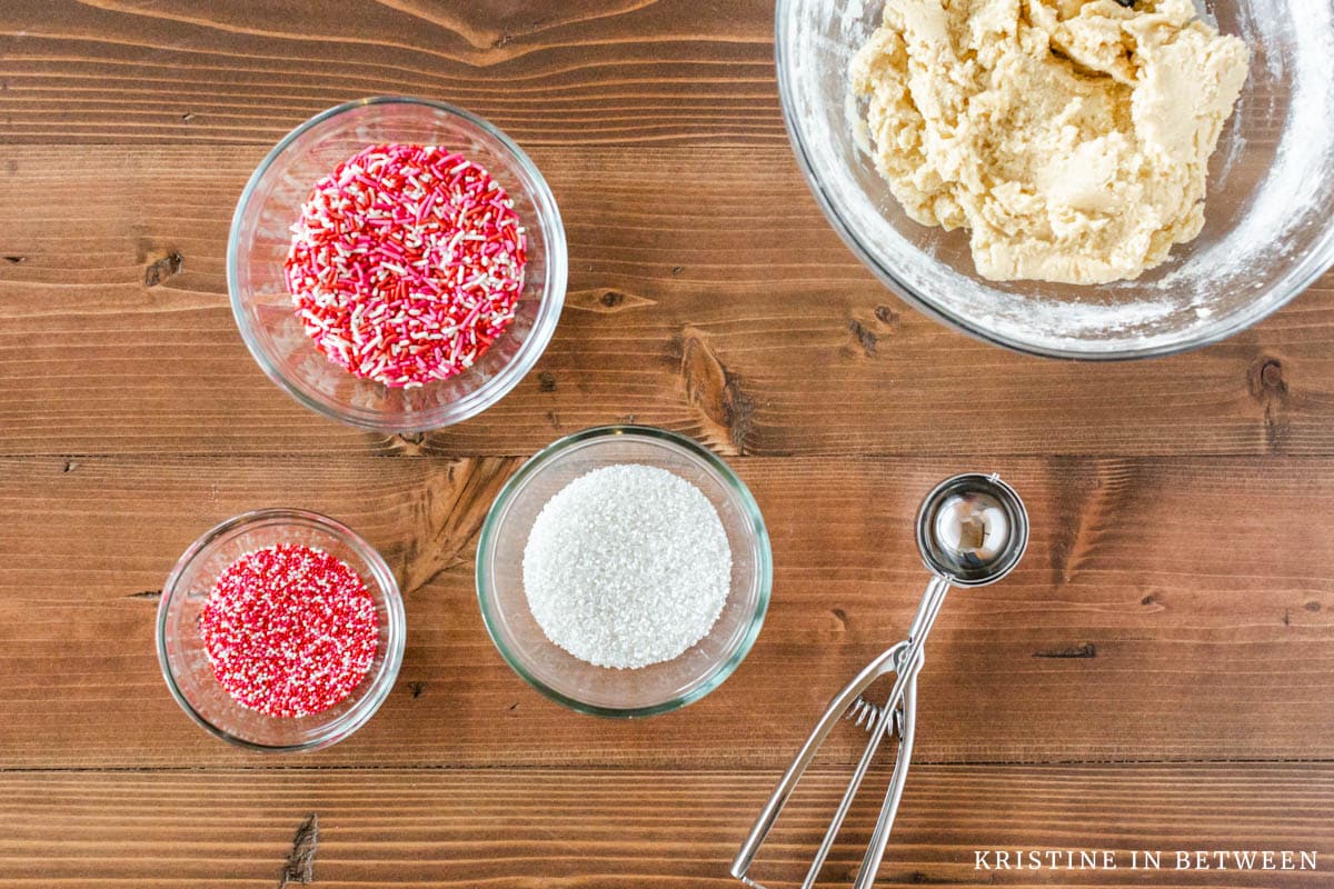 Three bowls of sprinkles with a cookie scoop laying next to them.