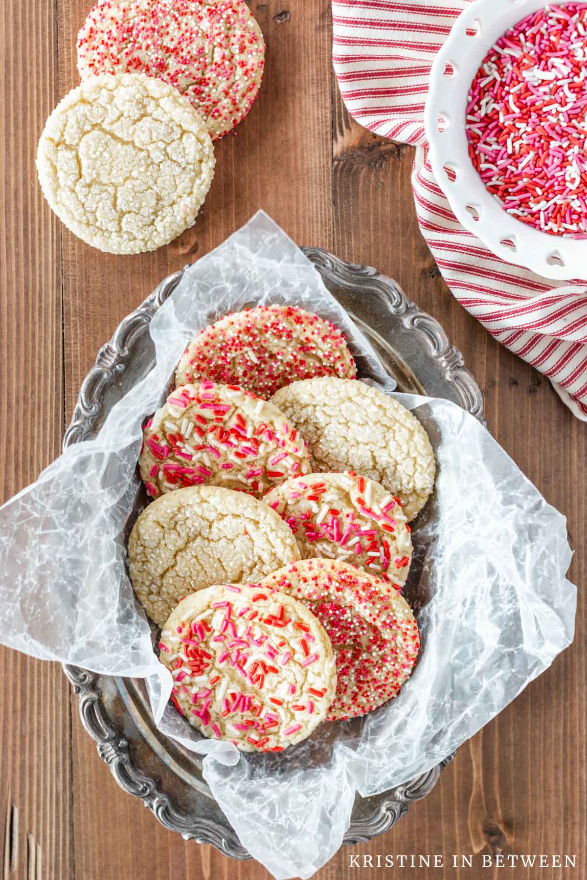 Valentine sugar cookies laying in antique tin bowl with sprinkles in the background.