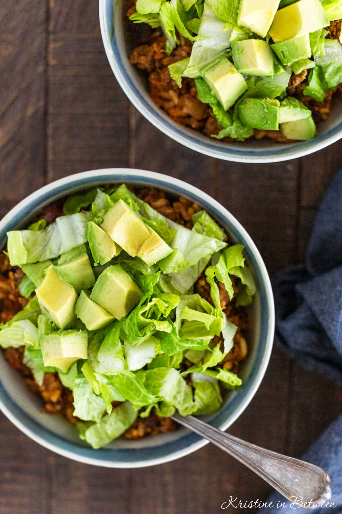 Two burrito casserole bowls with lettuce and avocado on top.