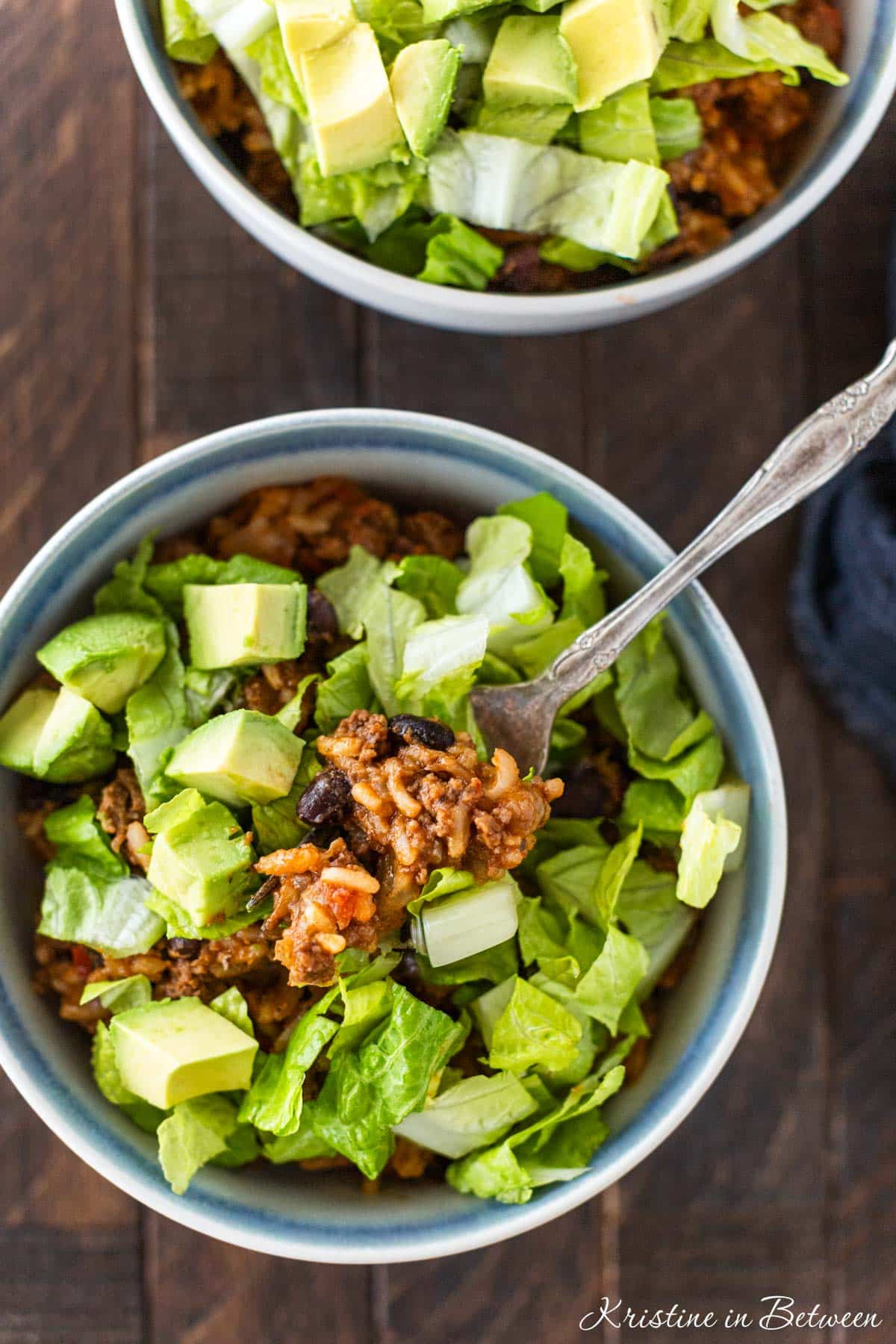 A bite of burrito casserole sitting on a fork with a blue napkin sitting next to it.