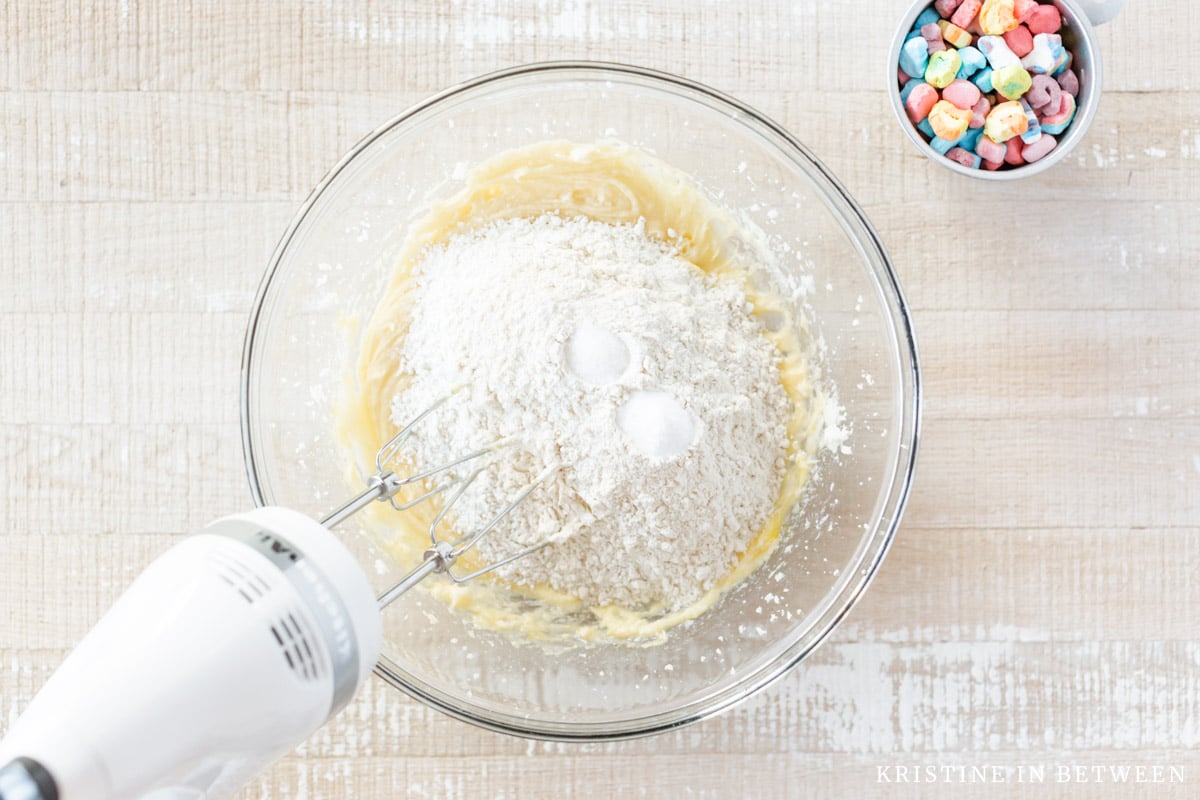 Flour, baking soda, and salt added to creamed butter in a glass bowl.