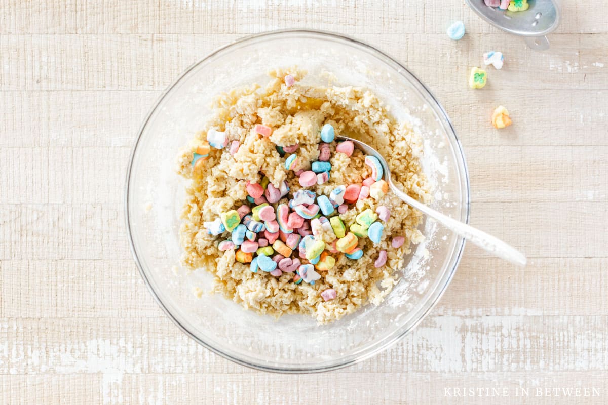 Lucky Charms added to cookie dough with an old spoon sitting next to it.